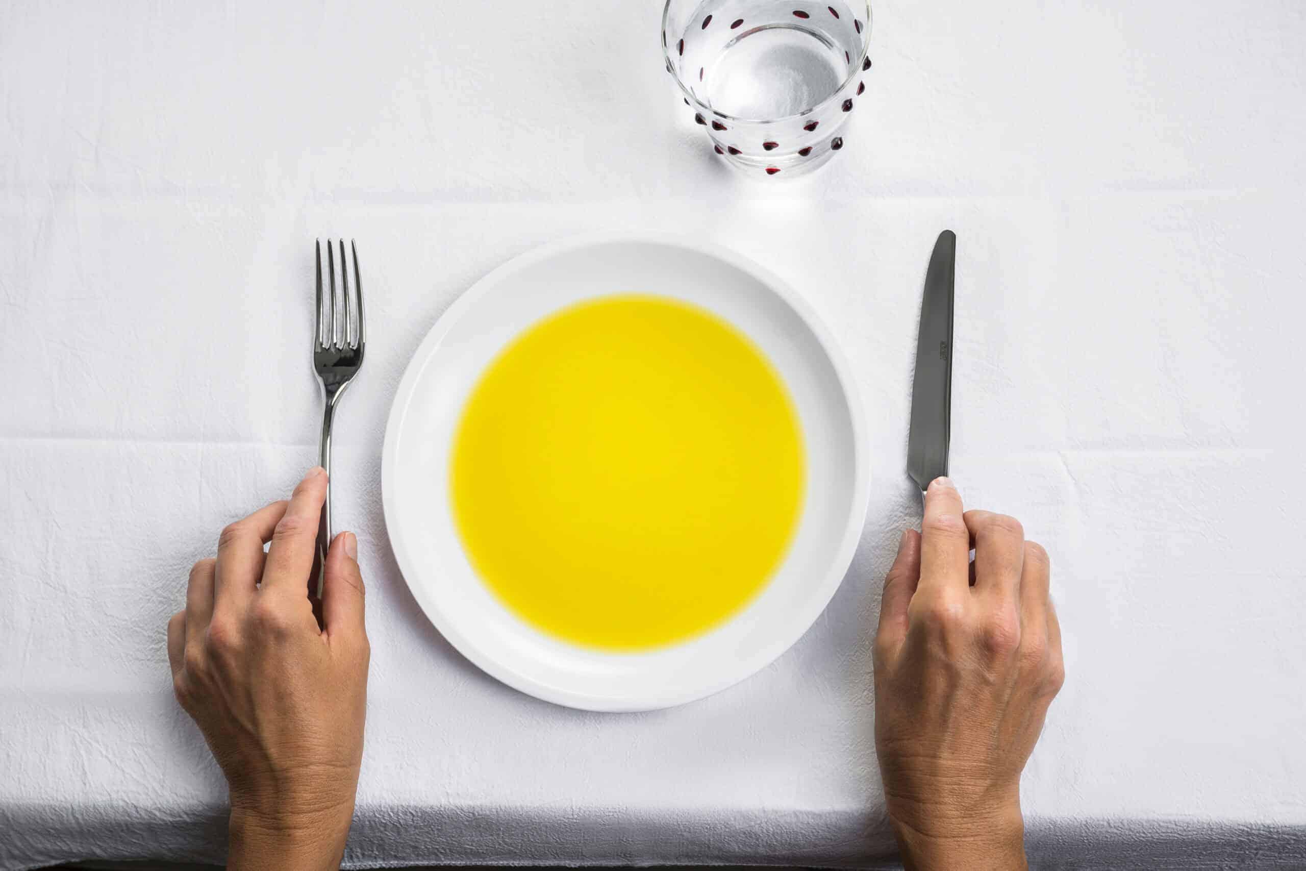 Piatto colmo di olio extravergine servito a tavola con forchetta e coltello