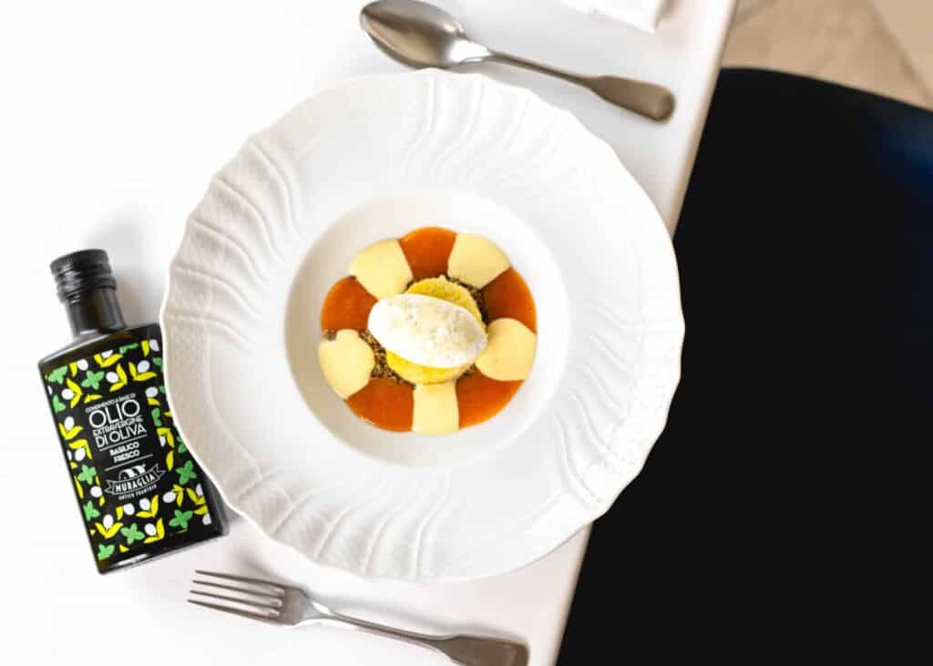 Bottiglia di olio extravergine Frantoio Muraglia accanto a un dessert impiattato con eleganza