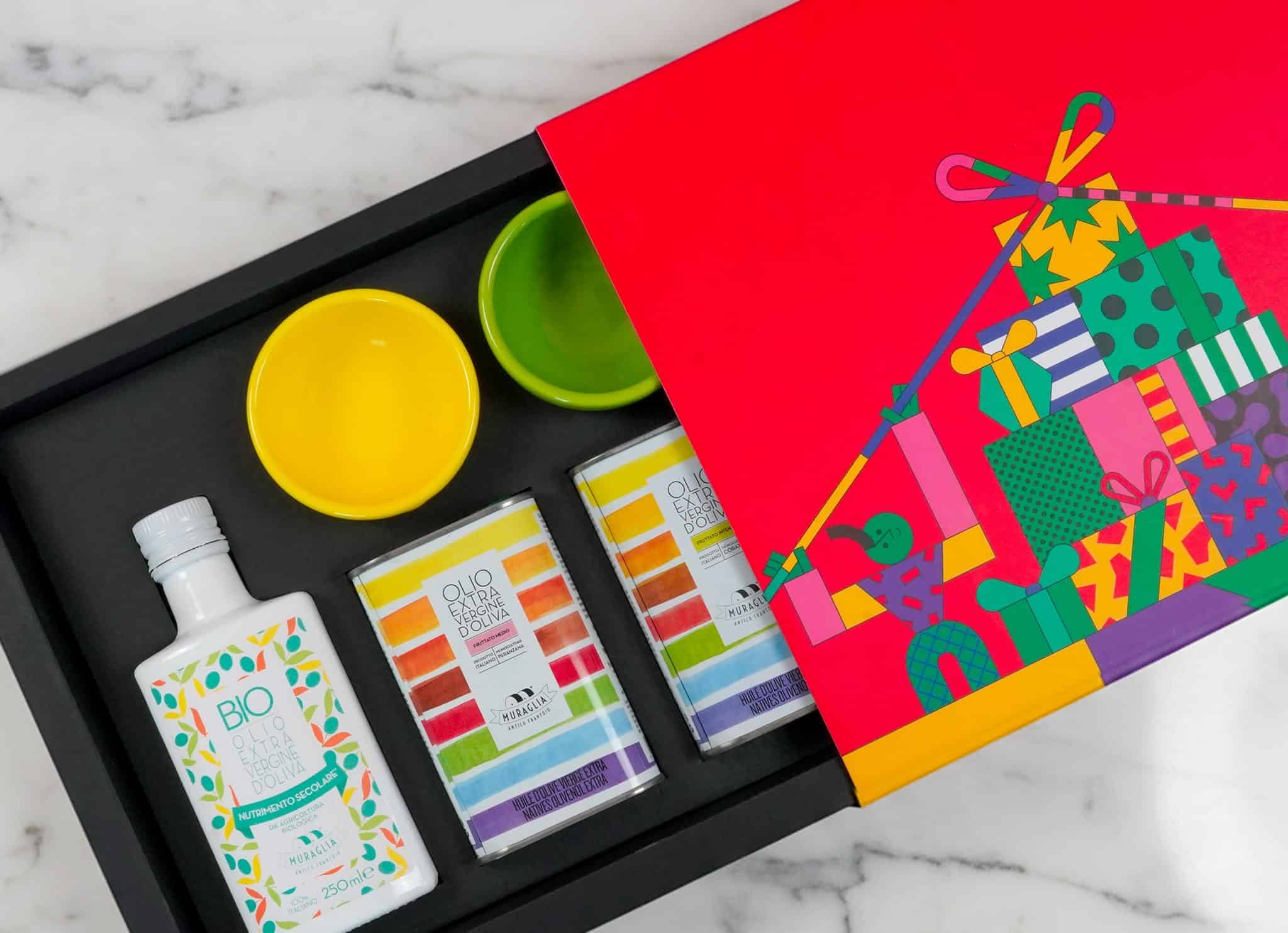 Confezione regalo aperta con bottiglia e lattine di olio extravergine e ciotole colorate